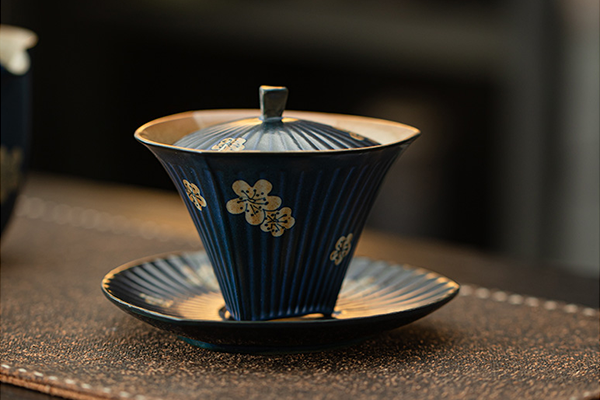 濃い青色の筋入りセラミック製蓋碗と受け皿のセット。淡い色の梅の花模様があしらわれている。