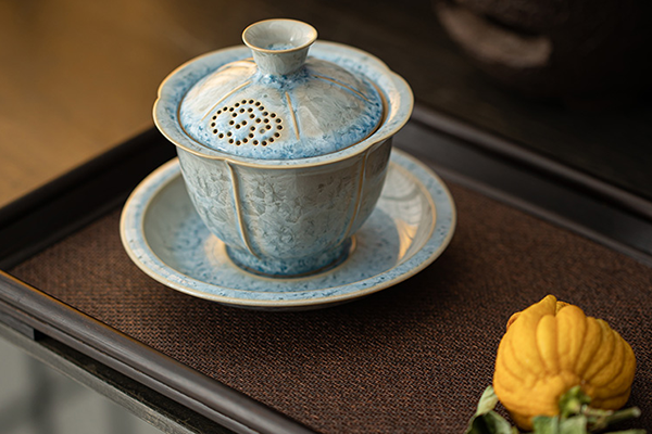 茶盤の上に置かれた、青い結晶釉の蓋碗セット。蓋には透かし彫りの穴があり、 옆には黄色い仏手柑が添えられている。