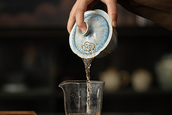 結晶釉の蓋碗から透明なピッチャーへお茶が注がれている様子。蓋には透かし彫りの穴が見える。