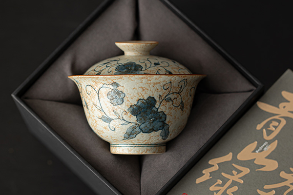 黒い箱の中に収められた、青花火石紅の唐草蓮文様が描かれた二才蓋碗。蓋が閉じられており、全体的にアンティークな雰囲気を持つ。