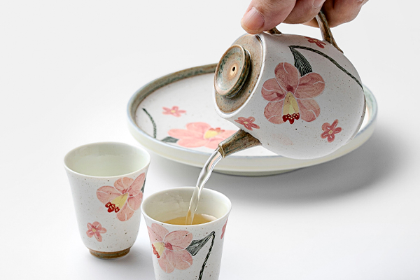 夕顔の花の急須から、湯呑みにお茶が注がれている瞬間。お茶の透明感と、陶磁器の温かみのある色が調和している。