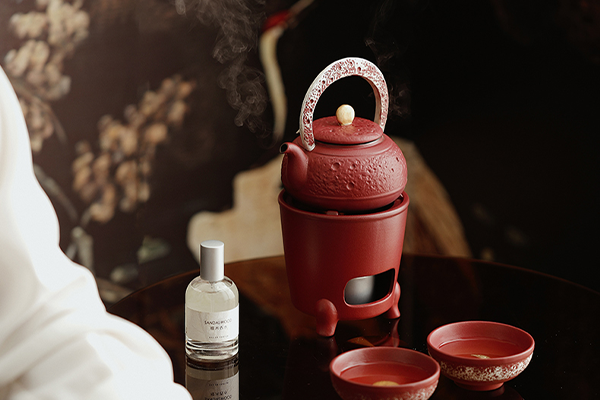 茶器セットが置かれたテーブル。提梁式急須が煮茶炉にセットされ、湯気が立ち上っている。手前には二つの茶碗があり、さらに香水瓶のようなボトルも見える。