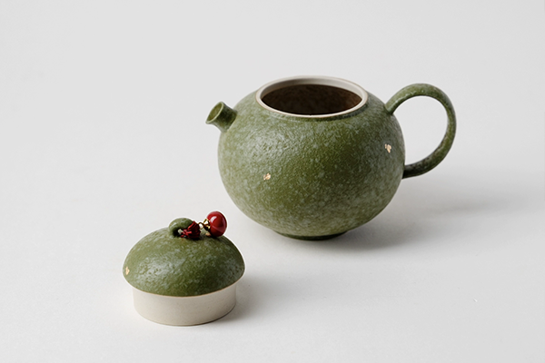 蓋を外した橘緑色の急須。本体の隣に置かれた蓋には、可愛らしい紅い実の飾りがついている。
