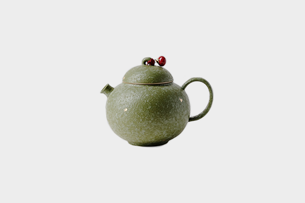 白い背景に置かれた、橘緑色の金彩急須。蓋には紅い実の飾りがついており、趣を添えている。