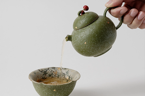 橘緑色の急須から、揃いの湯呑みにお茶を注いでいる場面。お茶の美しい水色が映える。
