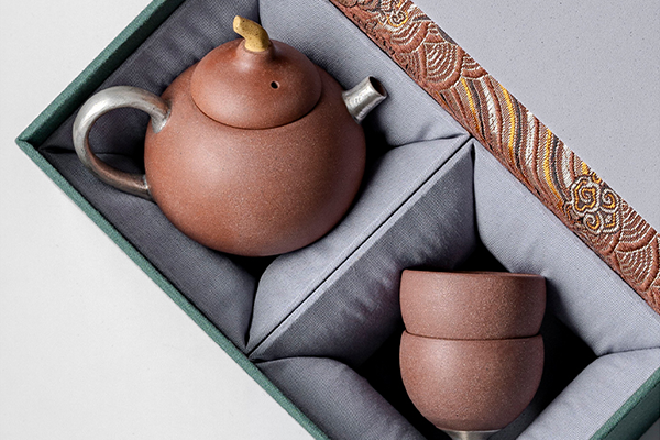 開いた箱に美しく収められた老岩泥と銀張りの茶器セット。梨の形をした急須と、二つの湯呑みが、丁寧に仕切られた空間に配置されている。