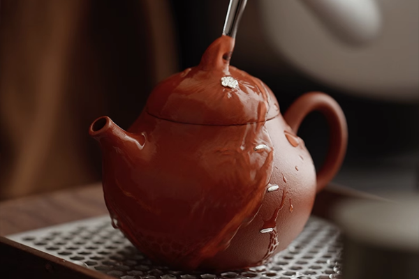 茶色の丸い急須に熱湯をかけて温めているクローズアップ。表面に水滴がついている。