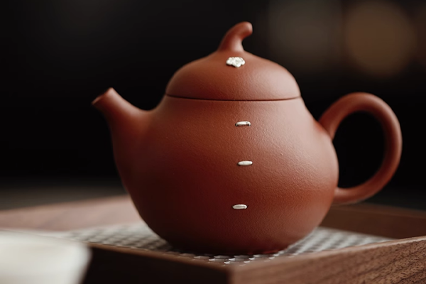 木製の茶托の上に置かれた、縦のラインと花の飾りがついた茶色の丸い急須。背景はぼけている。