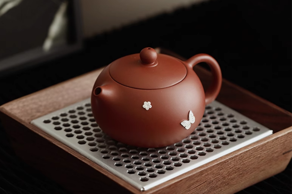 木製の茶托に置かれた、花と蝶の飾りがついた茶色の丸い丸い急須。