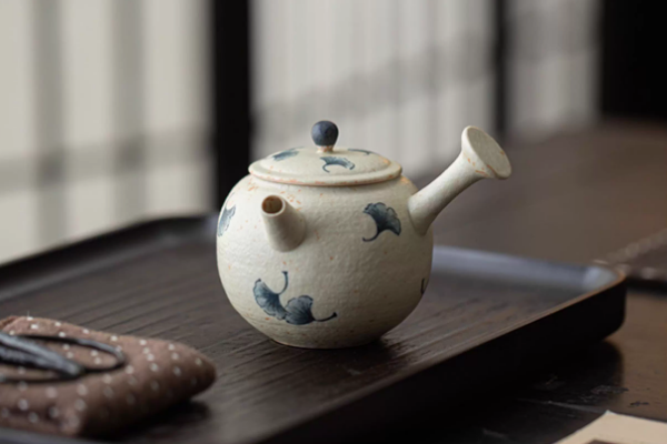 木製の盆の上に置かれた、青花・火石紅 手描き銀杏文様の急須。落ち着いた色合いの背景が、急須の美しいデザインを引き立てている。