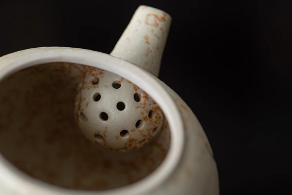 木製の茶托に置かれた、花と蝶の飾りがついた茶色の丸い丸い急須。