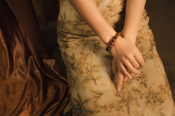 花柄のドレスを着た人物が、両腕を重ねて手を組んでいる。手首には、茶色いビーズとタイガーアイのビーズでできたブレスレットが着けられている。