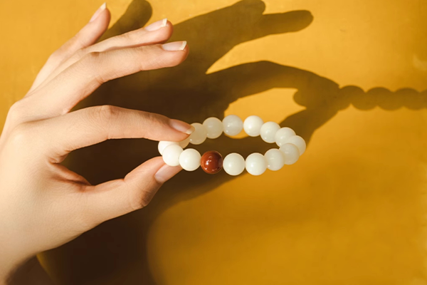 黄色い背景の前で、人物の手が白い菩提根ビーズと赤いナンホーン瑪瑙のビーズでできたブレスレットを持っている。強い光が当たっており、影がはっきりと写っている。