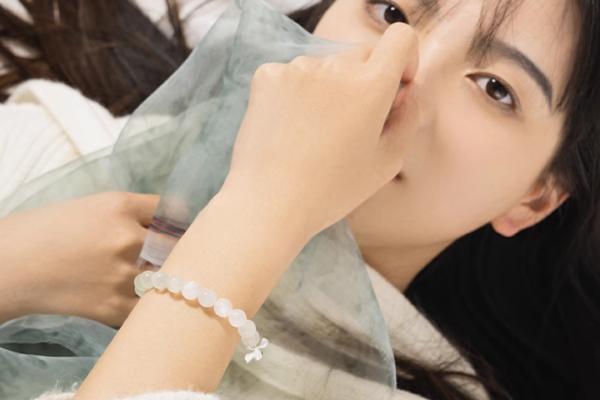 緑がかった半透明の布で顔の一部を覆う女性。手首には淡い緑色のビーズブレスレットが着けられており、かすかな光沢を放っている。