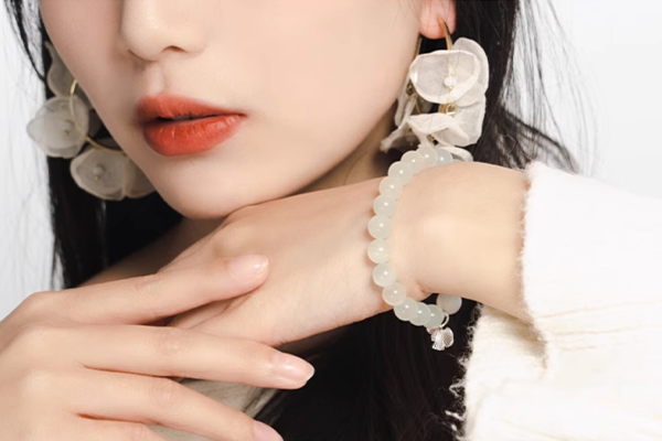白い服を着て、大きな白い花のようなイヤリングをつけた女性のクローズアップ写真。手首には、銀のイチョウの葉のチャームが付いた淡い緑色のビーズブレスレットが着けられている。