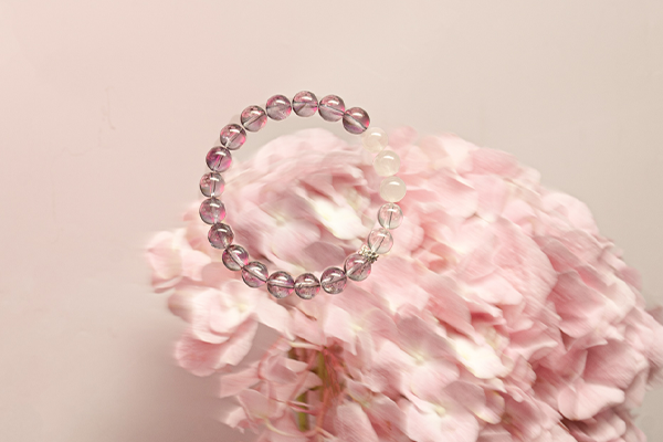 淡いピンク色のアジサイの花の上に、紫とピンクのビーズブレスレットが置かれている。